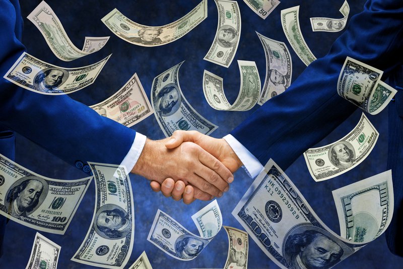 Two people shaking hands with money around them