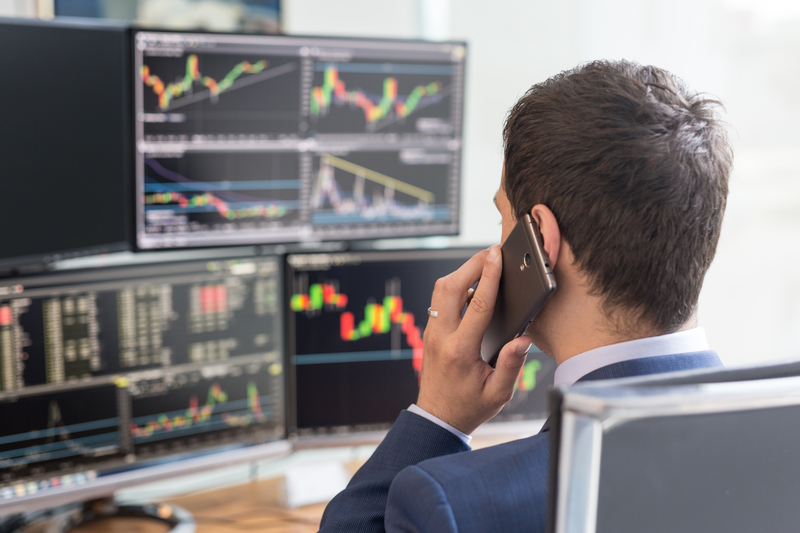 Over the shoulder view of computer screens ful of charts and data analyses and stock broker trading online.